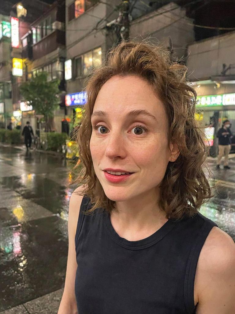 with a surprised expression on a neon-lit rainy Tokyo